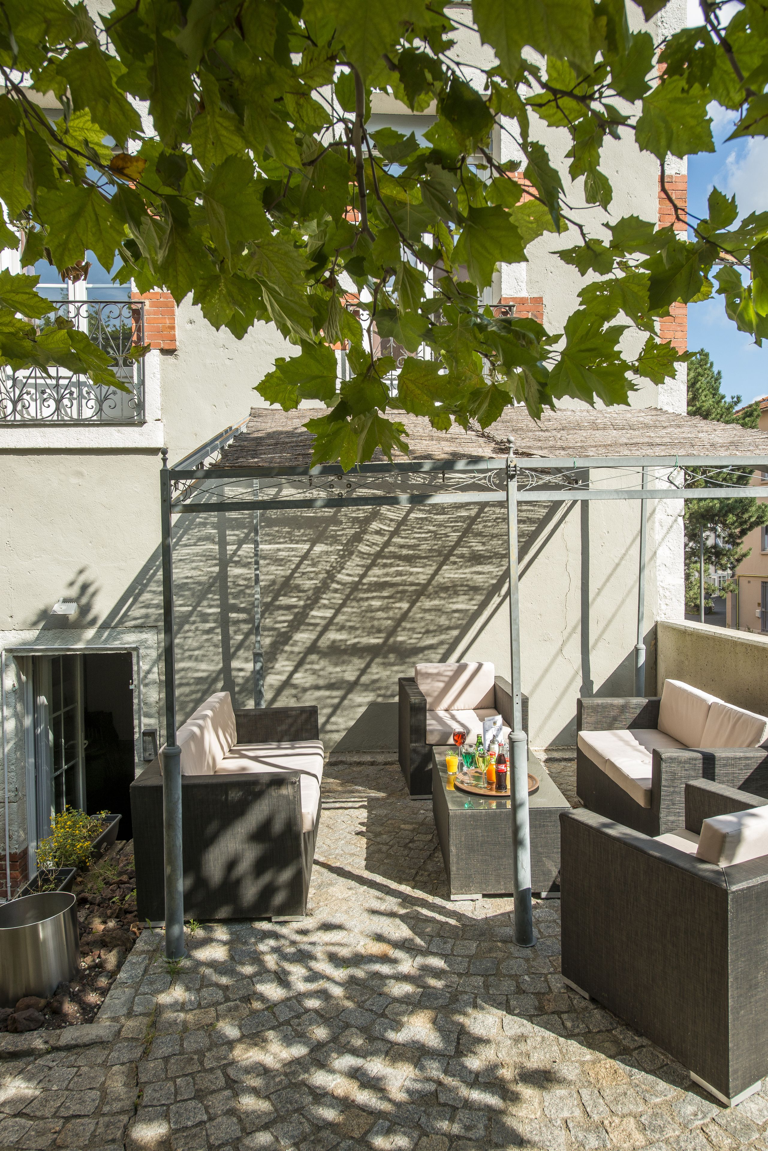 Un espace extérieur aménagé, abrité et doté d’une pergola, d’un sol en pierre et d’où l’on peut admirer un bâtiment en arrière-plan.