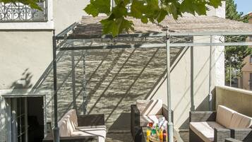 Un espace extérieur aménagé, abrité et doté d’une pergola, d’un sol en pierre et d’où l’on peut admirer un bâtiment en arrière-plan.