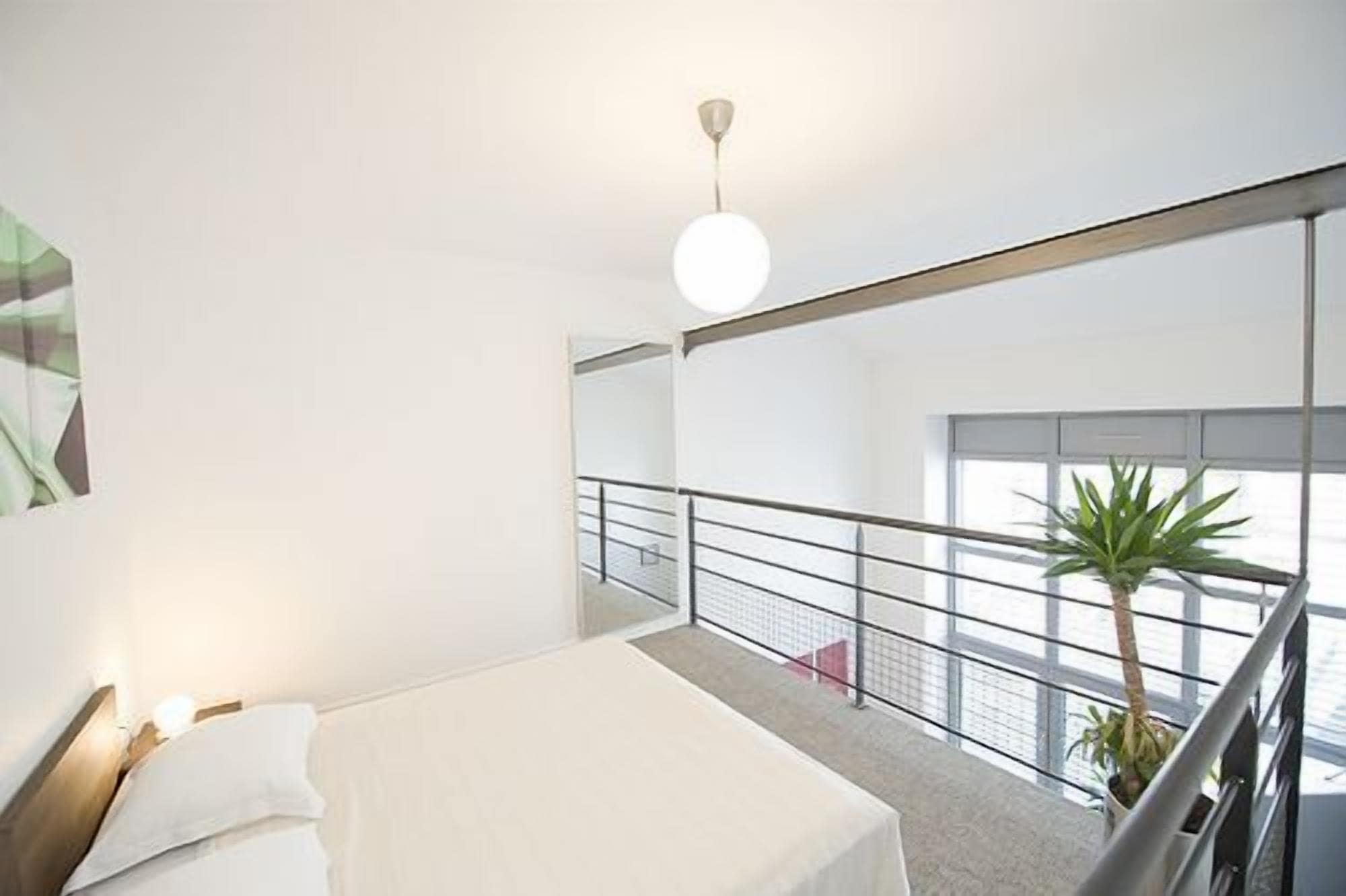 Ein modernes Hotelzimmer mit einem grossen Bett, Blick auf die Stadt durch raumhohe Fenster und einem Balkon mit Geländer.