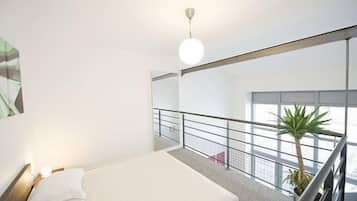 Una habitación de hotel moderna con una cama grande, vistas de la ciudad a través de ventanales y un balcón con barandilla.
