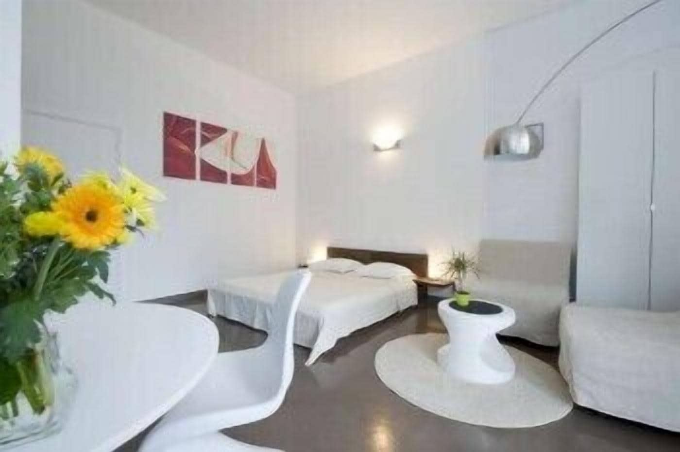 A modern hotel room with a bed, a white armchair, a small round table, and a potted plant.