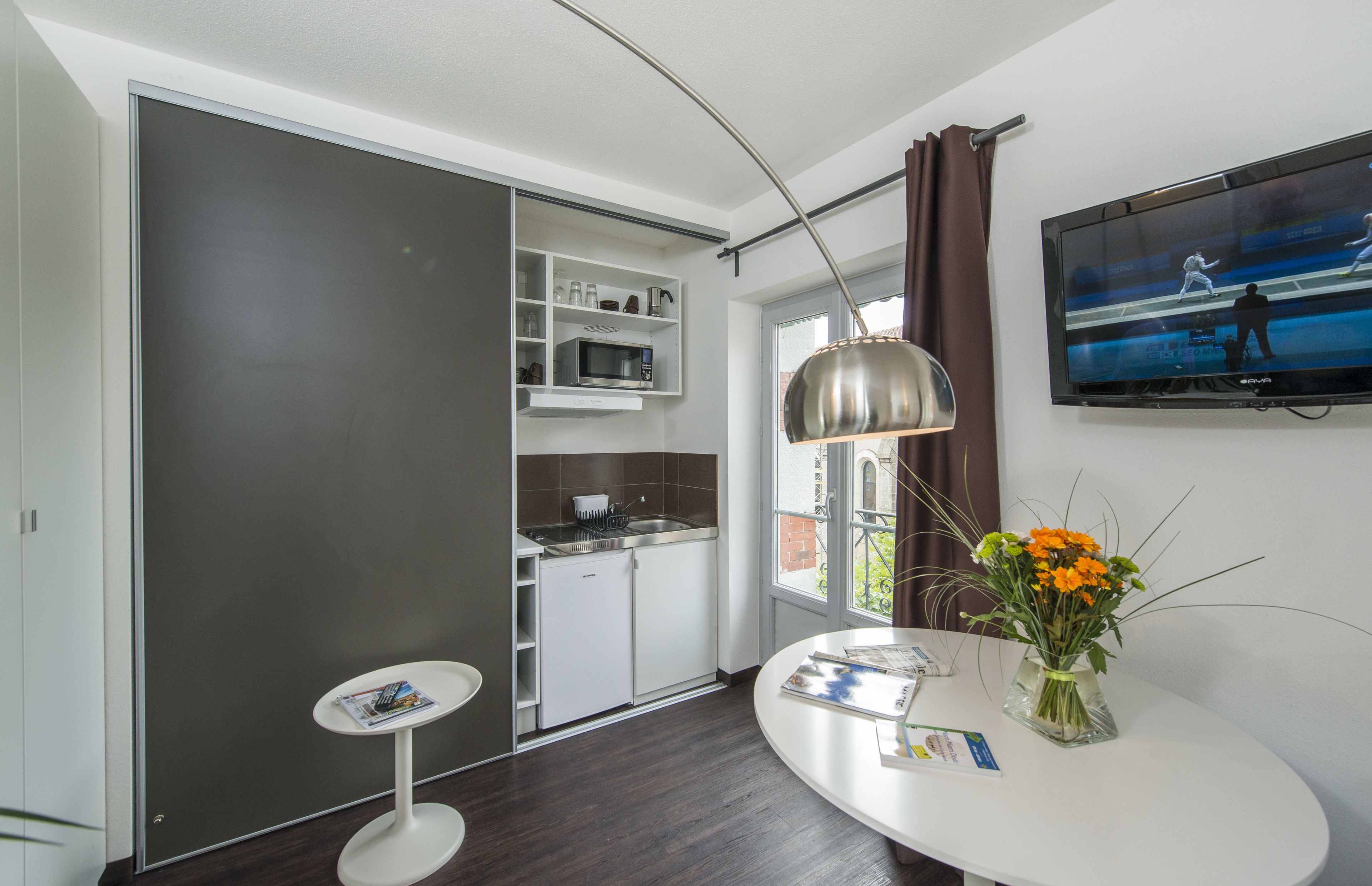 Een moderne keuken met witte kasten, een magnetron en een eethoek met een witte tafel en een bloevas.