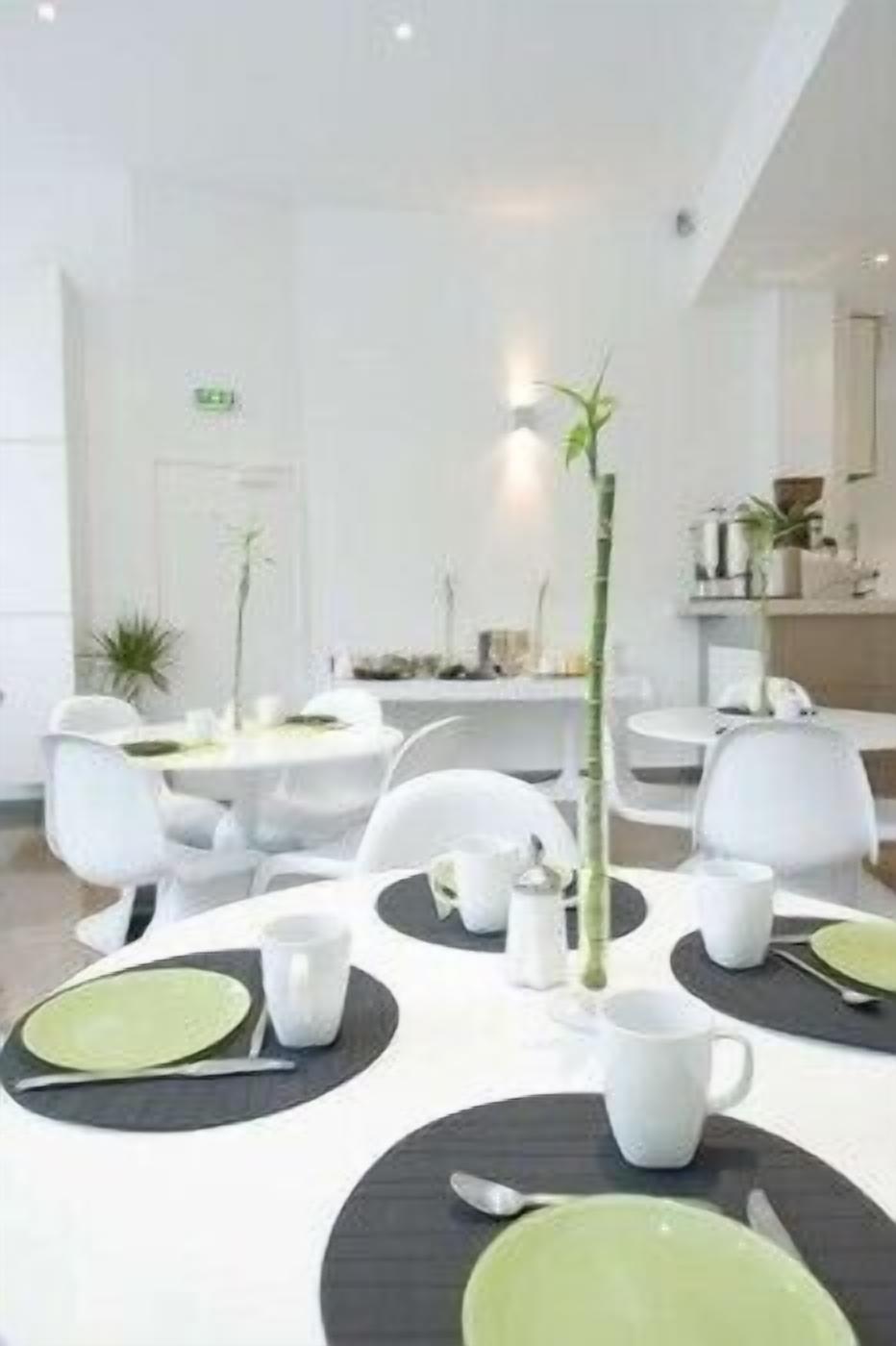 Un comedor moderno con mesas y sillas blancas, individuales negras y platos verdes.