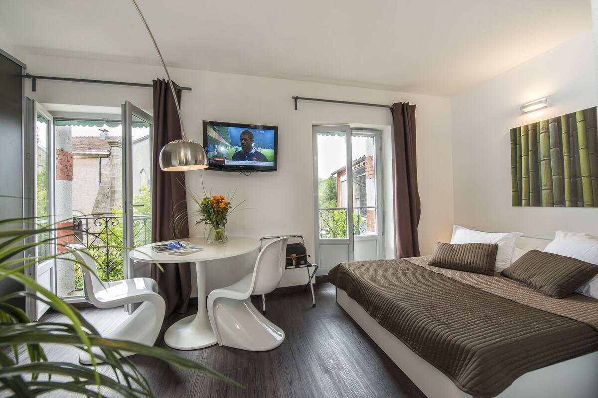 Une chambre d’hôtel moderne dotée d’un grand lit, d’un bureau avec une chaise, d’une télévision et d’un balcon offrant une vue sur la ville.