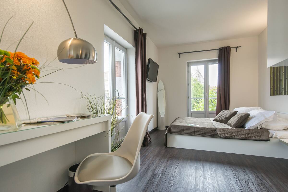 Une chambre à coucher avec un lit, un bureau, une chaise, un téléviseur et une fenêtre avec des rideaux.