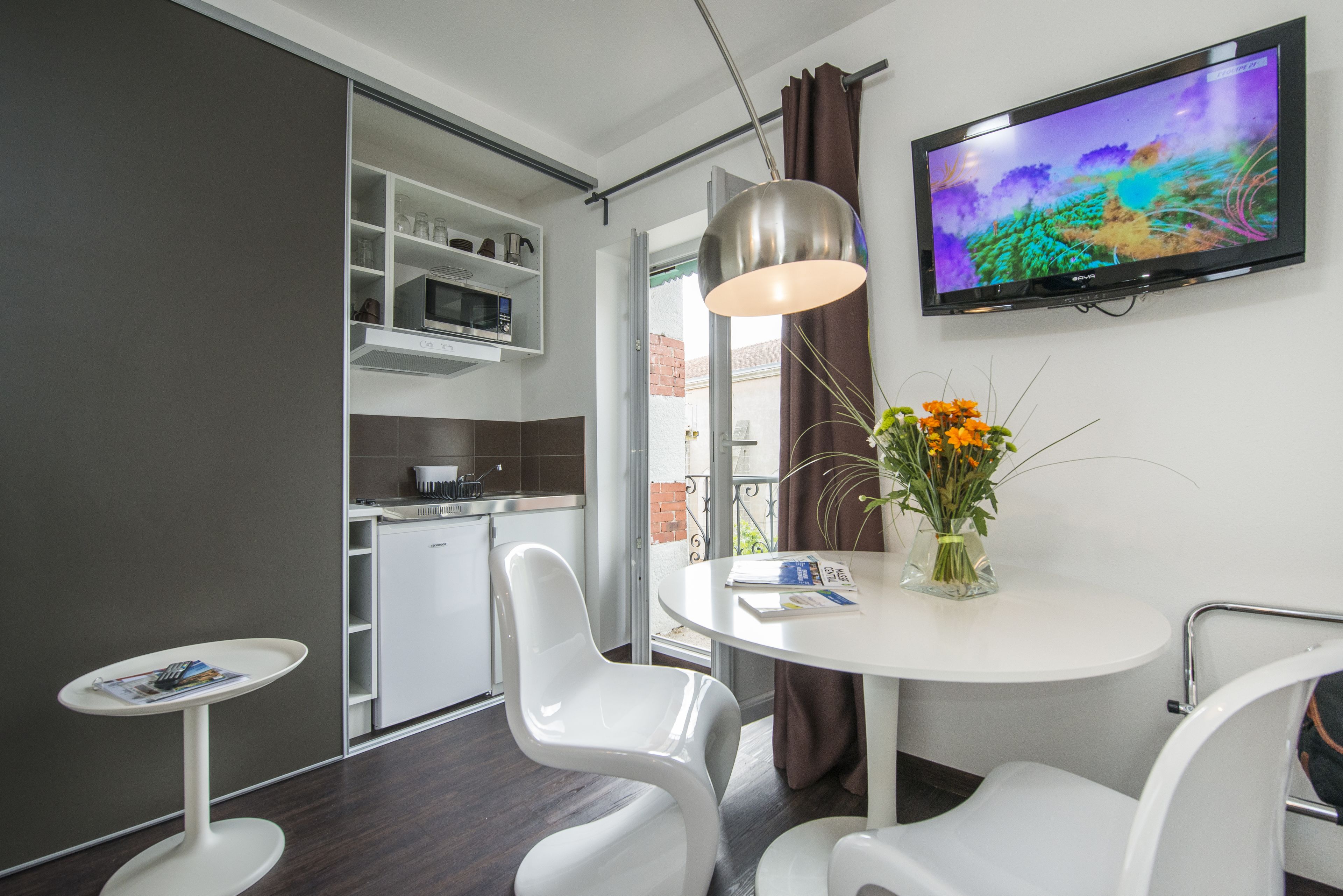 A modern hotel room with a dining area, a TV mounted on the wall, and a view of the outside.