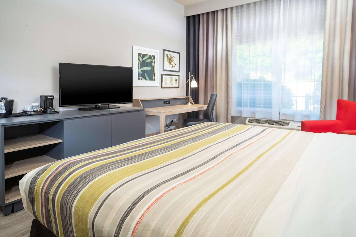 A hotel room with a bed, a desk with a computer, a TV, and a red chair.