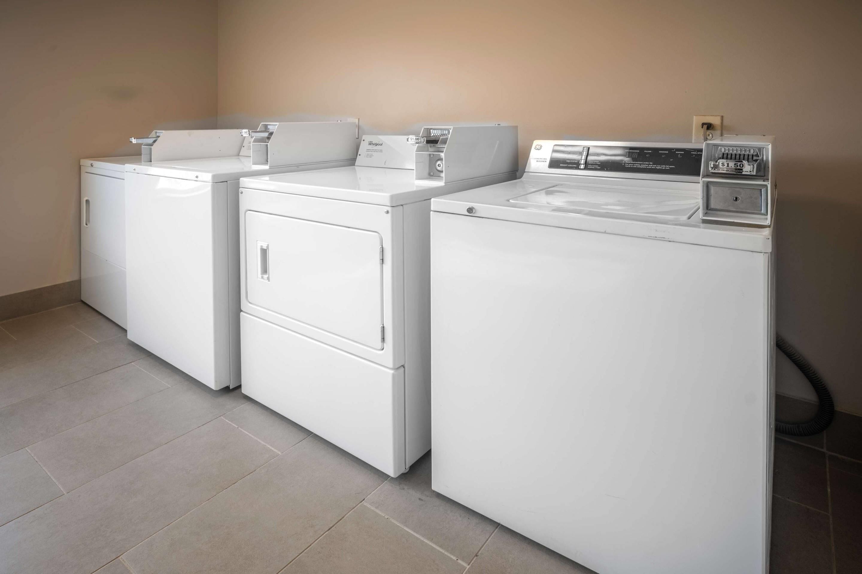 A laundry area with three stacked washers and dryers, a control panel, and a hose.