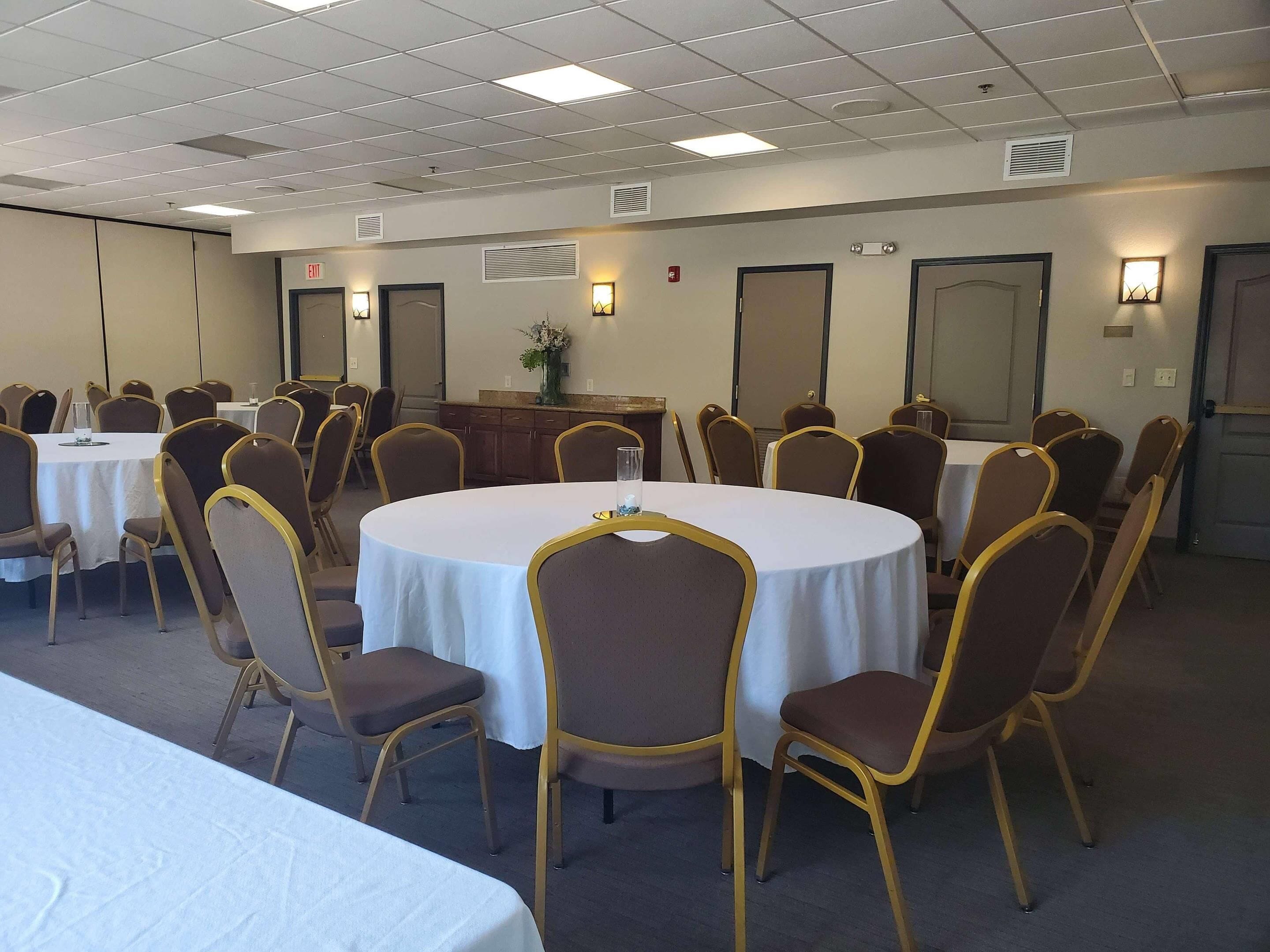 A conference room with round tables and chairs, equipped with ceiling lights and wall-mounted lamps.