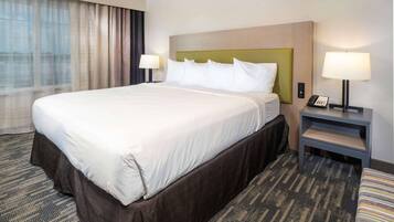 A hotel room with a large bed, two bedside tables with lamps, a carpeted floor, and a window with curtains.