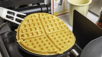 Een gaufreuset met een wafel erin, een spatel en een kopje op de achtergrond.