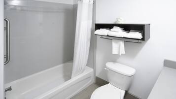 Een badkamer met een bad, douche, toilet en een plank met handdoeken.