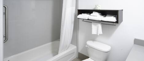 A bathroom with a bathtub, shower, toilet, and a shelf with towels.