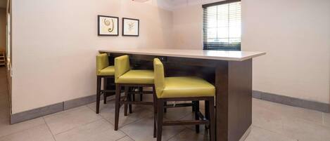 A modern kitchen with a bar area, two framed pictures on the wall, and a window with blinds.