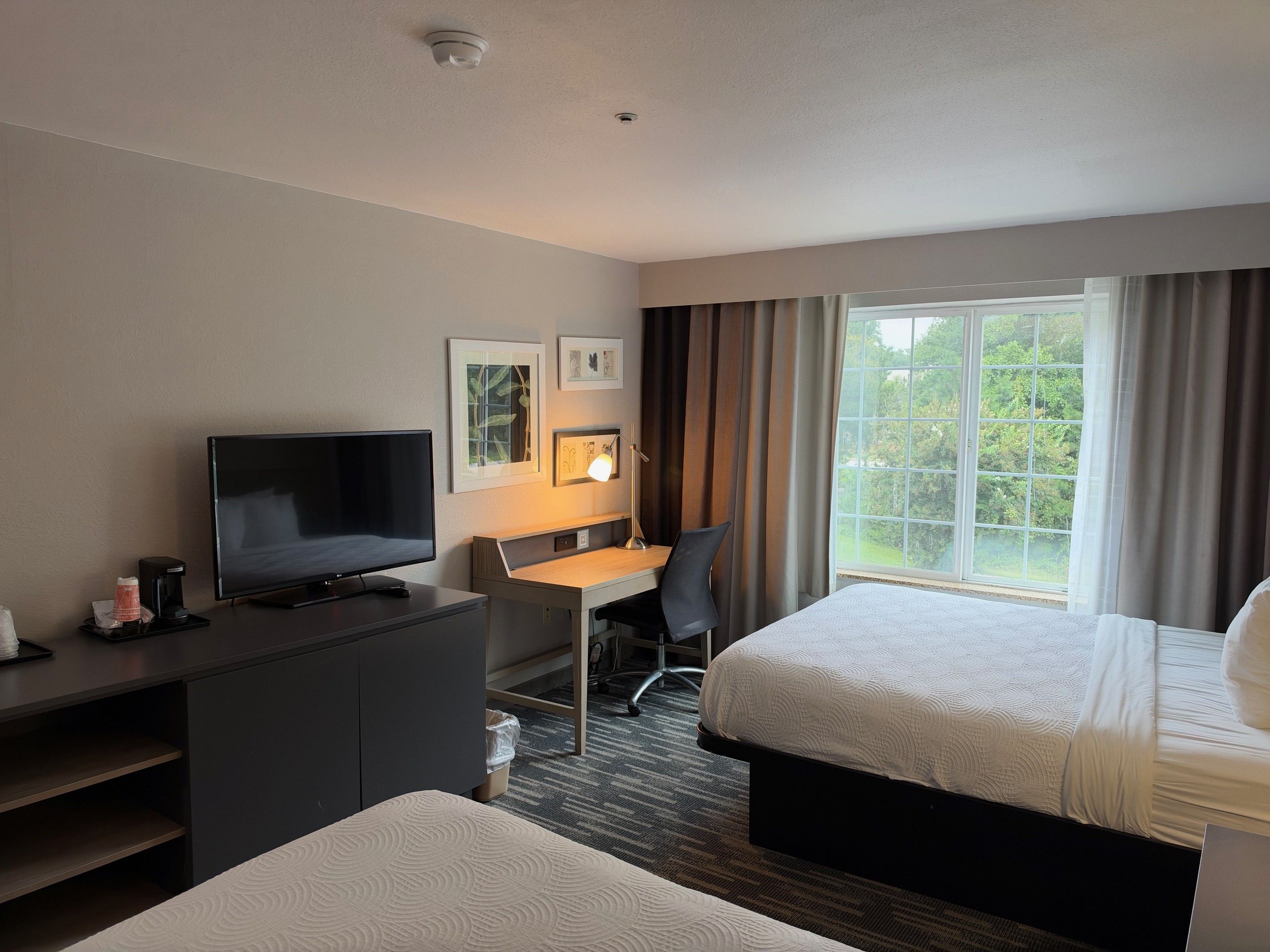 Una habitación de hotel con cama, escritorio con silla, televisor y ventana con cortinas.