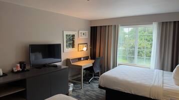 Una habitación de hotel con cama, escritorio con silla, televisor y ventana con cortinas.