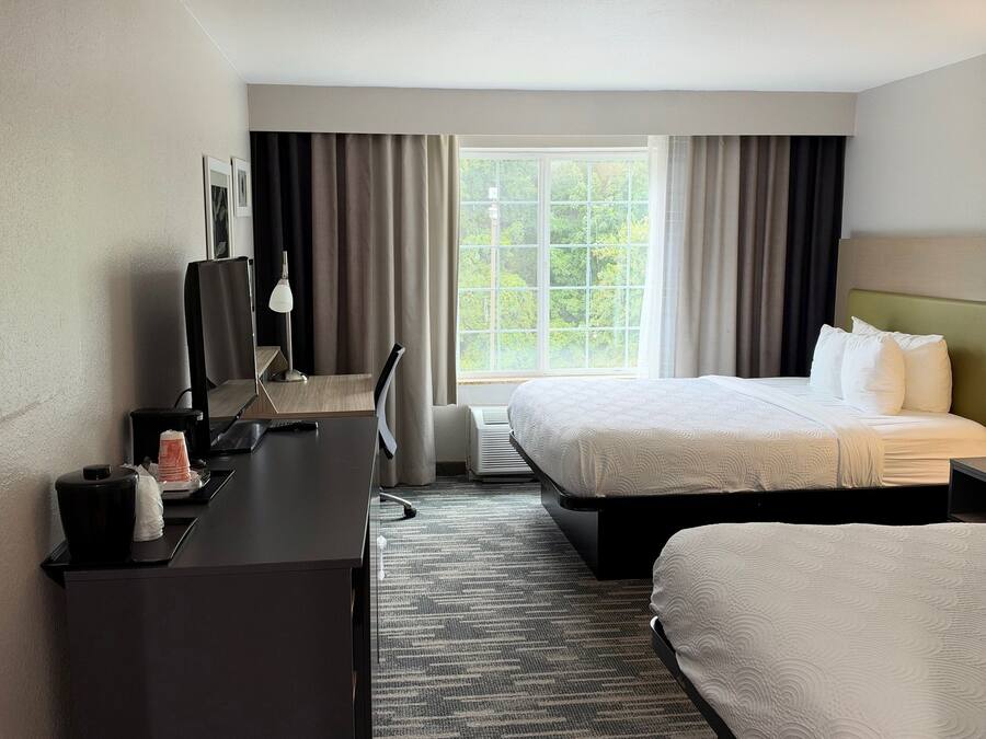 A hotel room with a desk, two beds, a window with curtains, and a ceiling light.