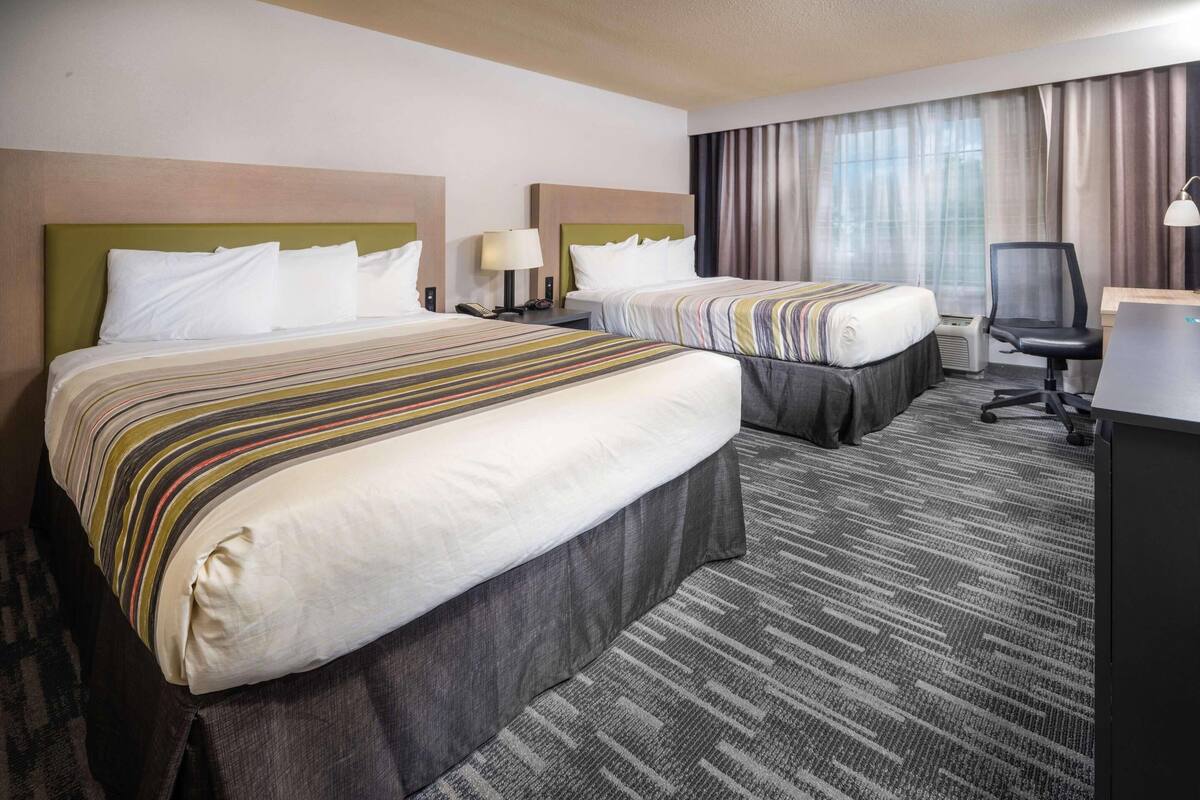 A hotel room with two beds, a desk, a chair, and a large window with curtains.