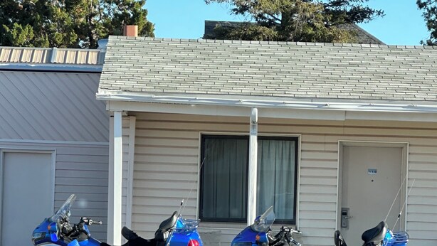 Two parked motorcycles in front of a building with a garage door and a window. - Canyonlands Motor Inn (Monticello)