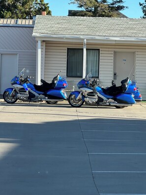 Two parked motorcycles in front of a building with a garage door and a window. - Canyonlands Motor Inn (Monticello)