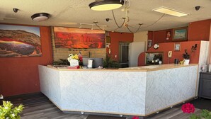A reception area with a marble counter, a large landscape painting, and a wooden floor. - Canyonlands Motor Inn (Monticello)