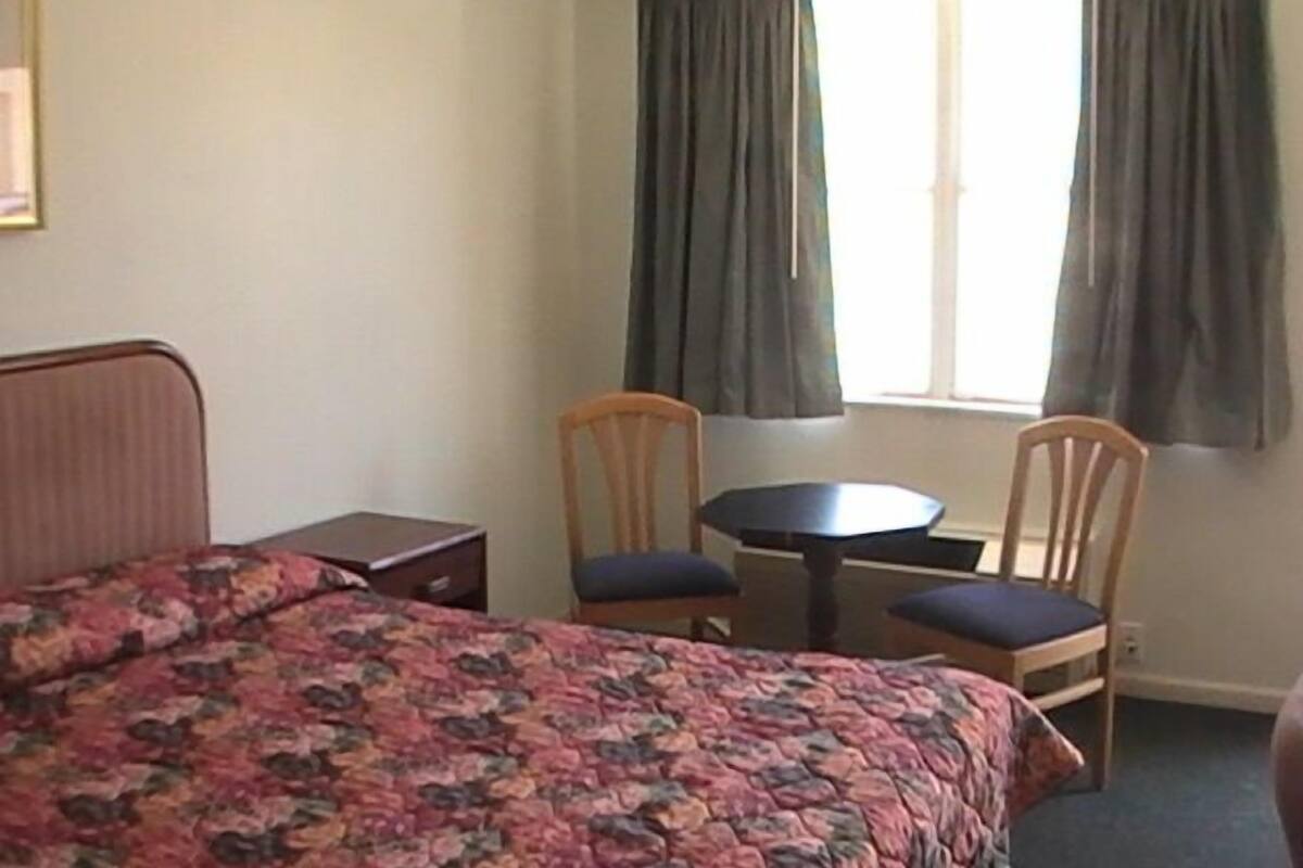 A bedroom with a bed, two chairs, a small table, and a window with curtains.