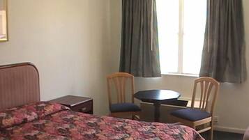 A bedroom with a bed, two chairs, a small table, and a window with curtains.