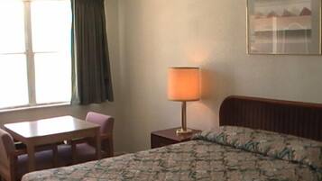 A hotel room with a bed, a desk, a chair, a lamp, and a window with curtains.