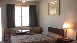 A hotel room with two beds, a small table, a chair, a lamp, and a window with curtains. - Hometown Inn Galion (Galion)