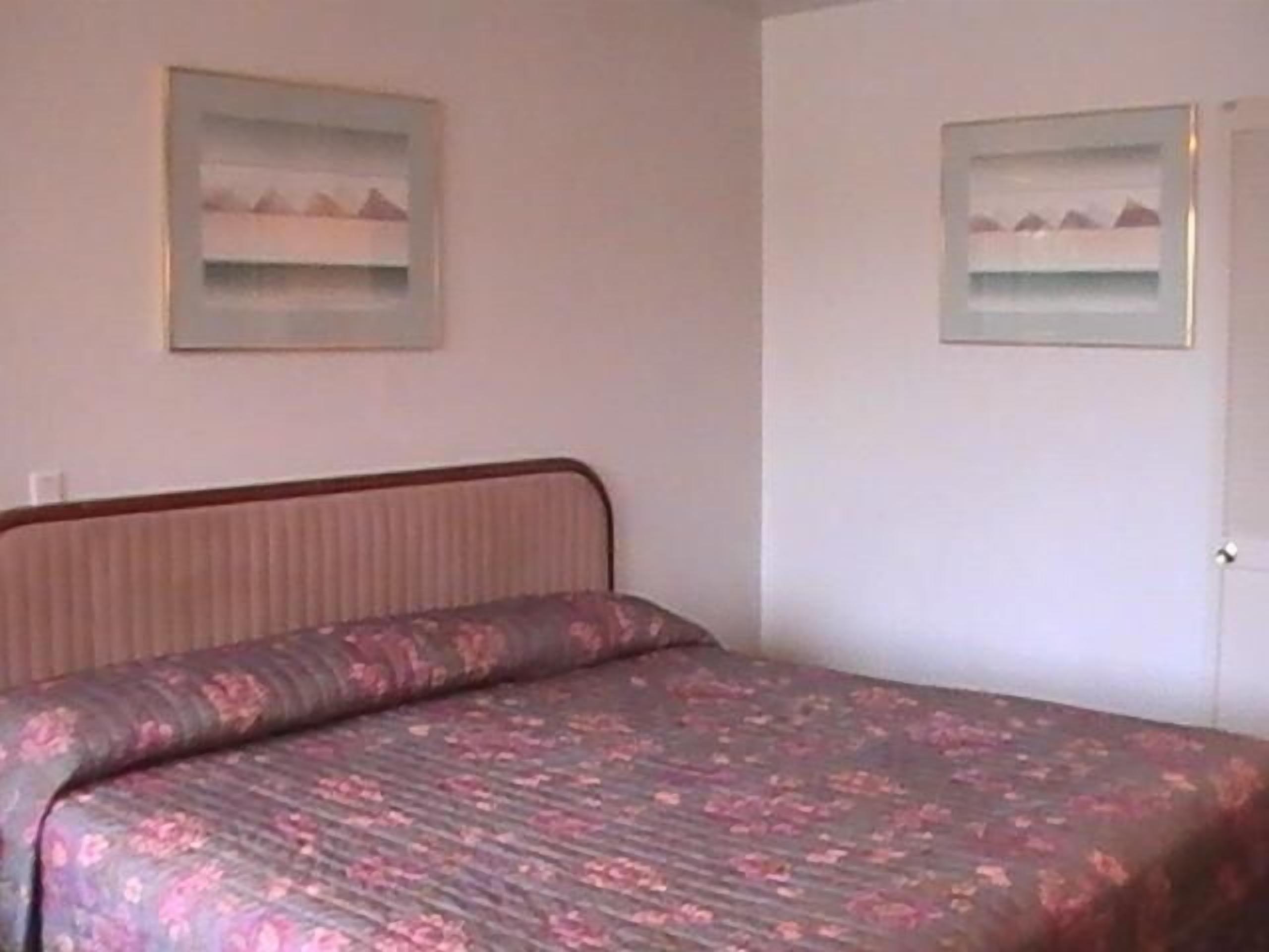 A bedroom with a bed, a headboard, and two framed pictures on the wall.