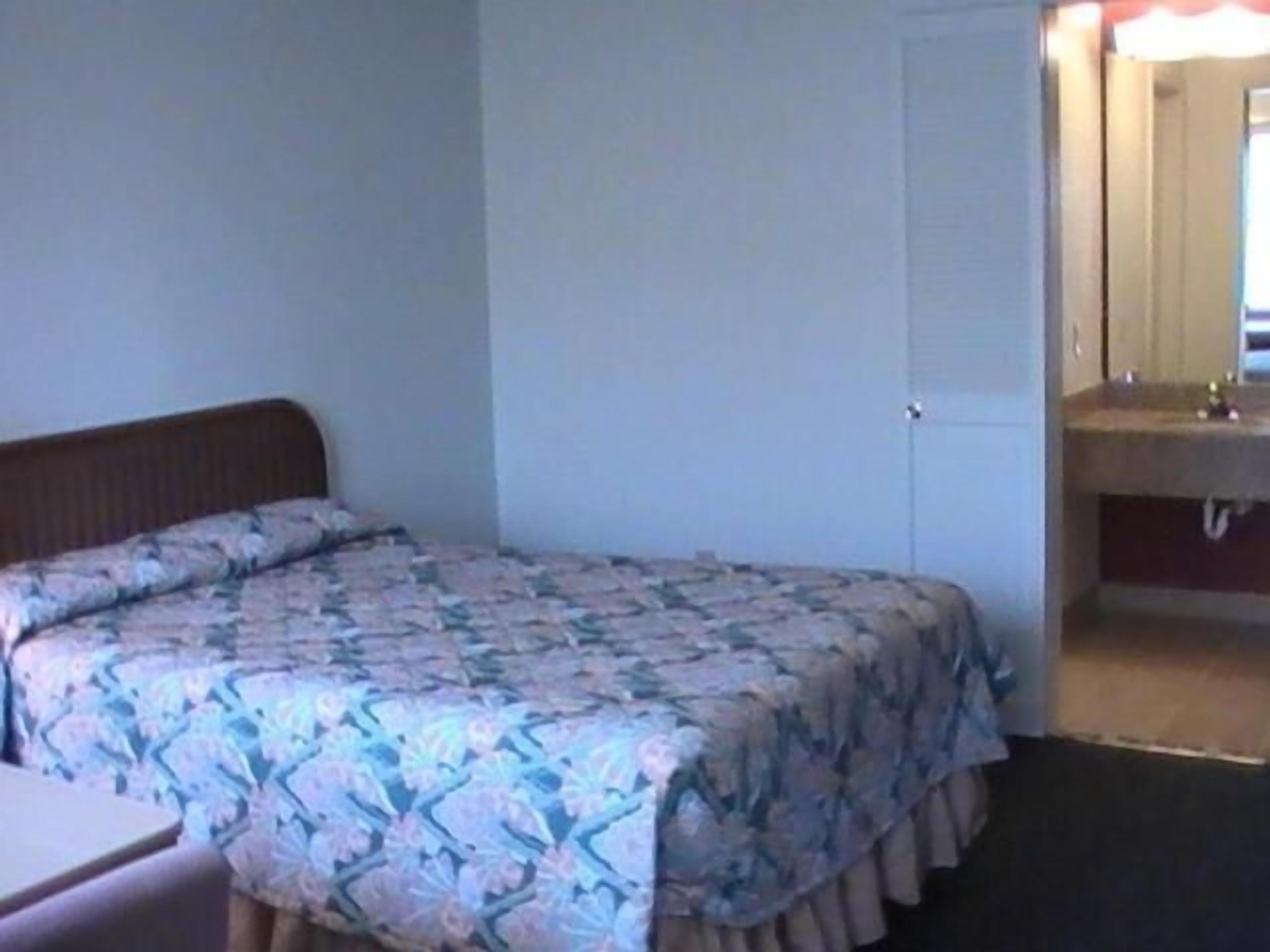 Una cama individual con una colcha estampada, una mesita de noche y un baño con lavabo y espejo.