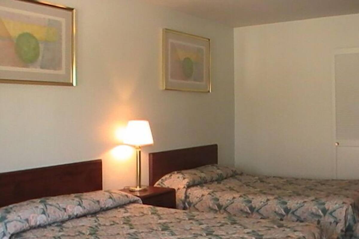 A hotel room with two beds, a nightstand with a lamp, and two framed pictures on the wall.
