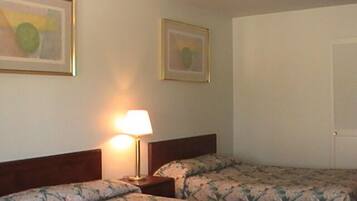 Une chambre d’hôtel avec deux lits, une table de chevet avec une lampe et deux tableaux encadrés au mur.
