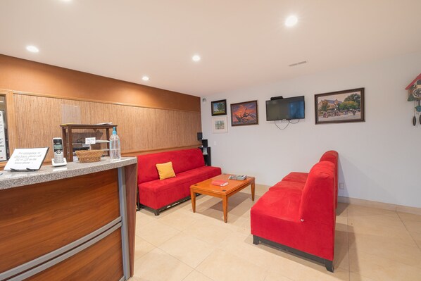 Un espace d’accueil avec un comptoir en bois, des canapés rouges, une table basse en bois et des tableaux encadrés accrochés au mur.