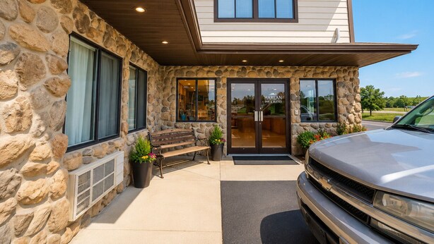 Fachada de piedra con un banco de madera, un coche estacionado adelante y la entrada de un edificio con un letrero que dice 'Harlan Inn & Suites'.