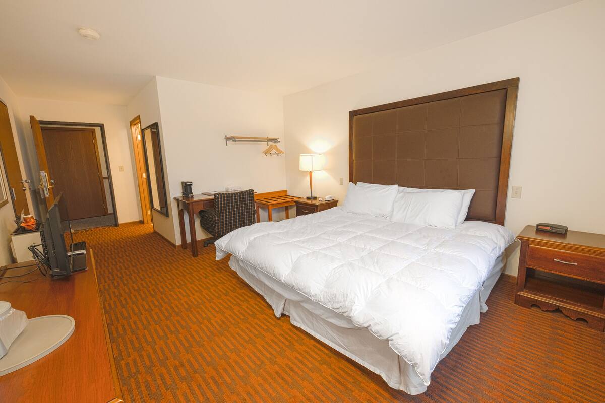Une chambre d’hôtel avec un grand lit, des tables de chevet, un bureau avec une chaise, une lampe et un téléviseur.