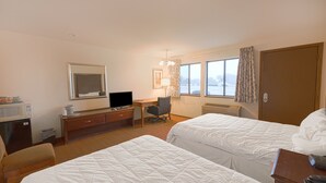 Habitación de hotel con dos camas, un escritorio con computadora, una silla, televisor y ventana con cortinas.