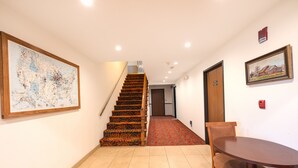 Un pasillo con una escalera de madera, una mesa de comedor con sillas y un mapa enmarcado en la pared.