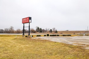 Señal del Harlan Inn & Suites en un entorno rural, con un campo de césped y árboles al fondo.