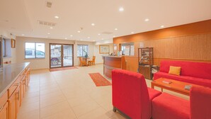 Un amplio vestíbulo de hotel con un sofá rojo, un mostrador de recepción de madera y un gran ventanal con vistas al exterior.