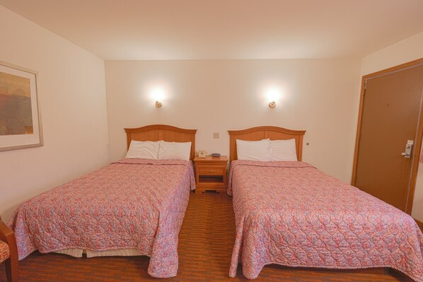 A room with two single beds, wooden headboards, bedside tables, and a nightstand with a lamp.