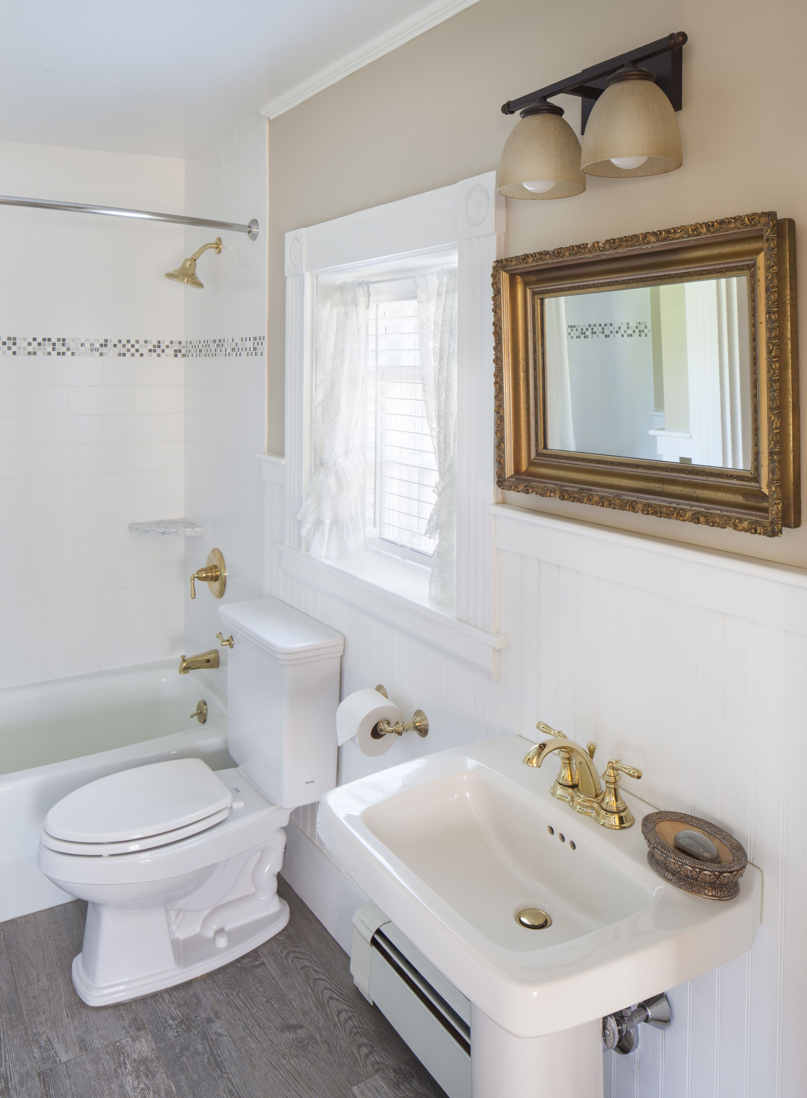A bathroom with a bathtub, toilet, sink, and a mirror with a decorative frame.
