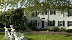 A white house with a brick pathway leading to the front door, surrounded by greenery and a lawn. - Captain's House Inn (Chatham)