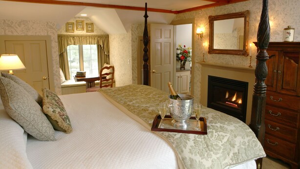 A four-poster bed with a champagne bucket and glasses, a fireplace, and a mirror above it. - Captain's House Inn (Chatham)