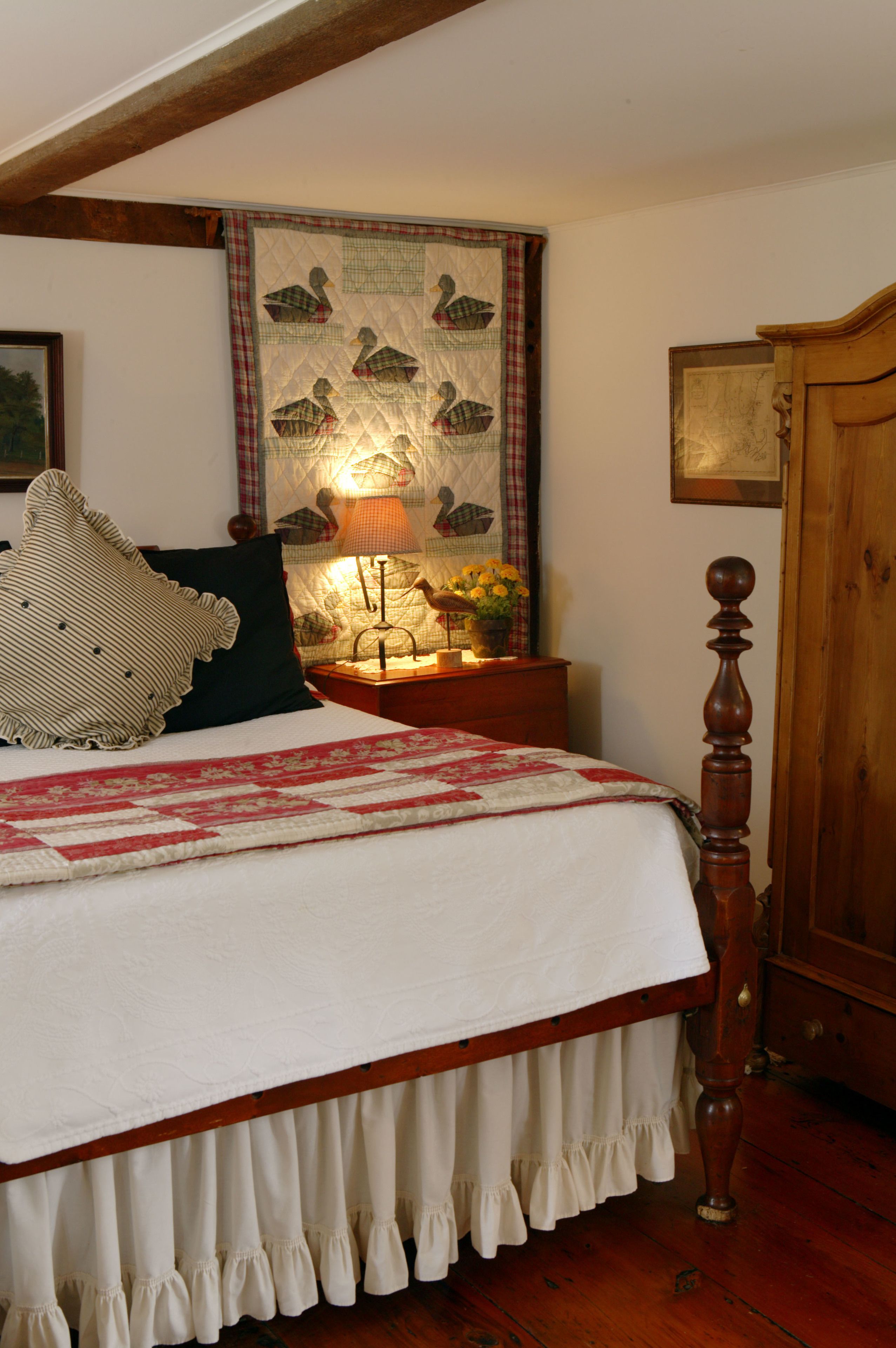 A bedroom with a wooden bed frame, a quilted headboard, a bedside table with a lamp, and a wall hanging.