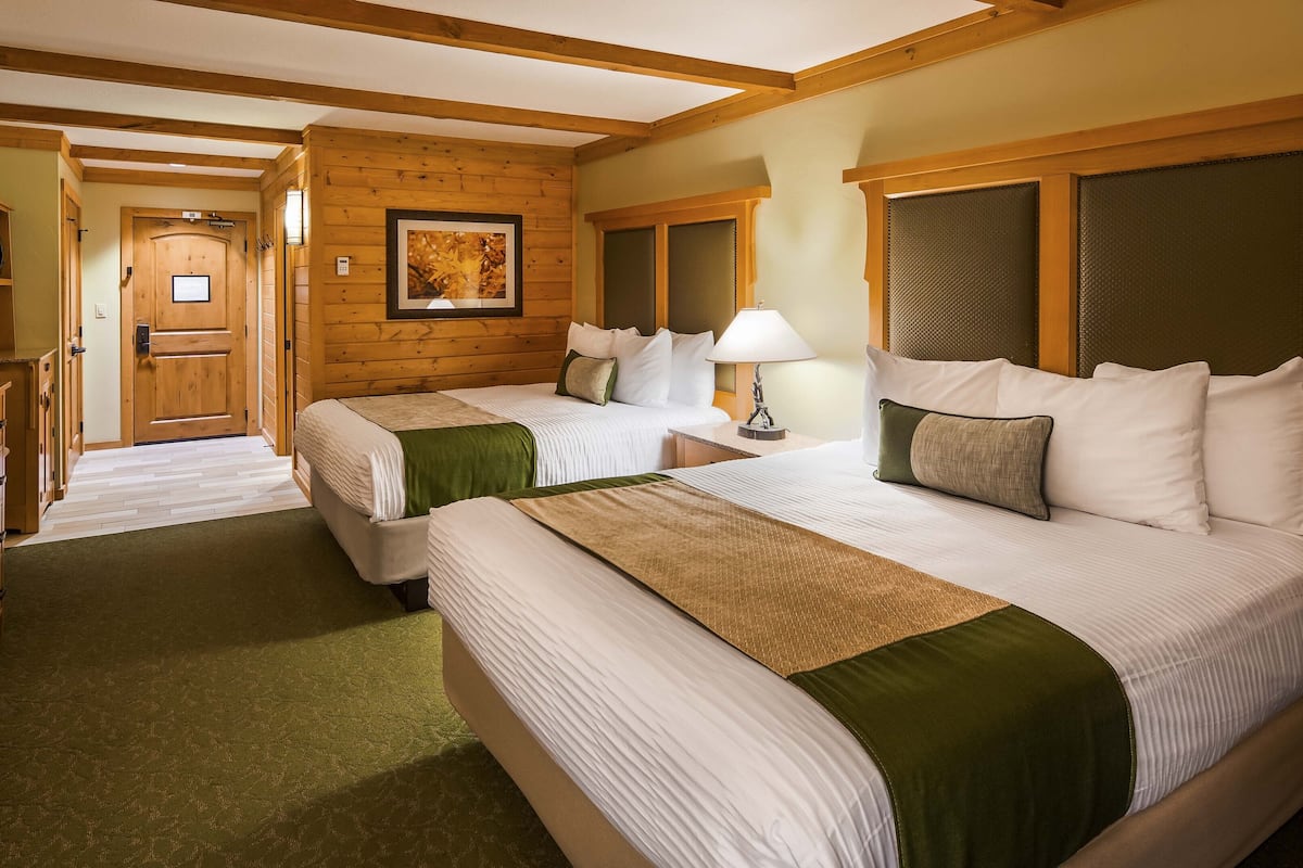 A hotel room with two beds, a television, wooden walls, and a framed picture on the wall.