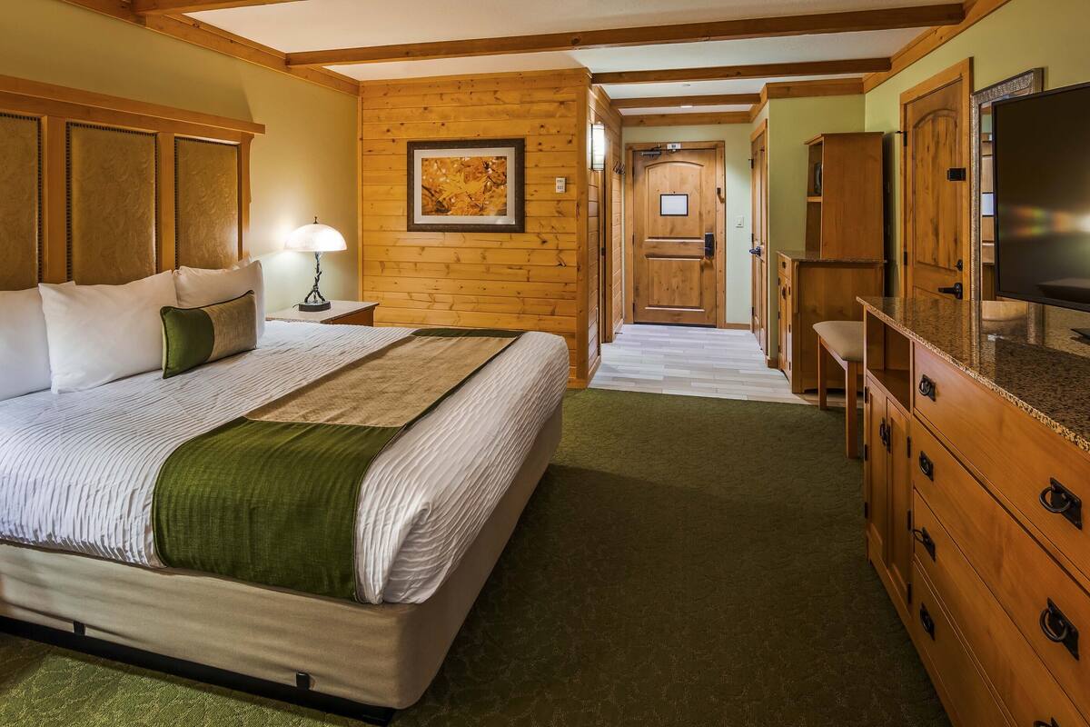 A hotel room with a large bed, wooden headboard, a television, and a wooden cabinet.