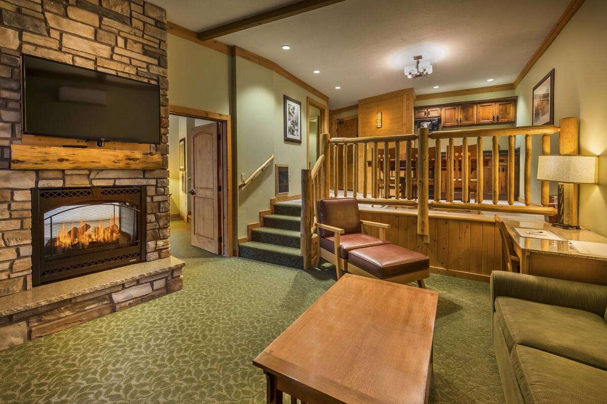A cozy living room with a stone fireplace, a staircase leading to a second floor, and a bar area.