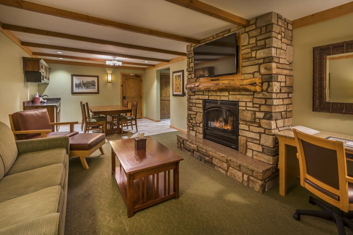 A cozy living room with a stone fireplace, wooden furniture, and a television mounted on the wall.