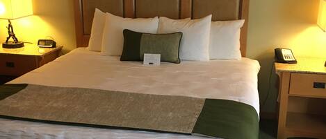 Una cama bien hecha con cabecera, dos mesitas de noche con lámparas y un teléfono junto a la cama.